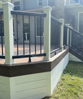 White metal railing on a raised backyard deck, bordered by green grass, with wooden steps leading to a house.
