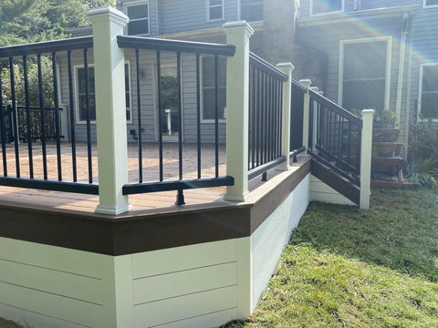 White metal railing on a raised backyard deck, bordered by green grass, with wooden steps leading to a house.