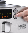 Super Automatic Espresso Machine With One Touch Brewing Delivers Solid Daily Grinds And Straight Fire Shots That Hit Different Every Time In A Sleek Silver Body Made For Zero Hassle Home Brewing, control panel close-up with hand pressing button.