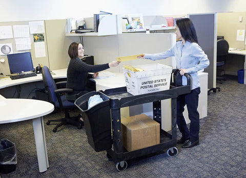 Two women exchanging mail at an office with a Top Tier Heavy Duty Two Shelf Utility Cart With Durable Structural Foam Lipped Trays.
