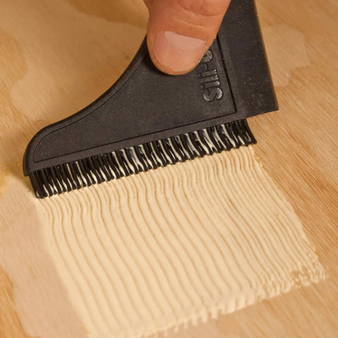 Person using squeegee from Non Stick Wood Glue Brush Silicone Applicator Kit With Comb Squeegee And Tray on wood surface.