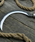 Hand-Forged Large Sickle With 7.5 Inch Blade, High-Carbon Steel For Gardening, Harvesting, And Landscaping, Ergonomic Ash Handle For Reduced Fatigue, Pro Grade Tool on rustic wooden background with rope.