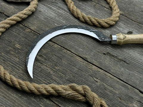 Hand-Forged Large Sickle With 7.5 Inch Blade, High-Carbon Steel For Gardening, Harvesting, And Landscaping, Ergonomic Ash Handle For Reduced Fatigue, Pro Grade Tool on rustic wooden background with rope.