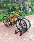 Durable Bike Floor Stand For Garage Parking And Storage, Fits 22-28 Inch Wheels, holding two mountain bikes on a pathway