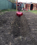 Hiller Furrower Kit for Rear Tine Tillers with Adjustable Wing digging a furrow in garden soil, rust-colored tiller visible