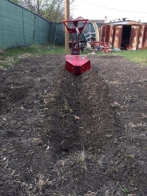 Hiller Furrower Kit for Rear Tine Tillers with Adjustable Wing digging a furrow in garden soil, rust-colored tiller visible