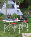 Portable Go To Camp Kitchen With Large Food Prep Area Folding Outdoor Kitchen For Camping Tailgating And Grilling Includes Side Table Utensil Hooks And Mesh Storage set up in a campsite with tent and lantern.