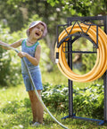 Heavy Duty Outdoor Garden Hose Holder With 5 Spikes And Basket in use, child playing with hose, freestanding black metal stand
