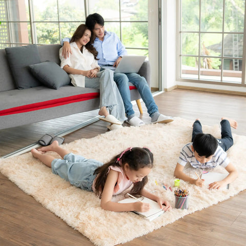 Family relaxing on sofa and children drawing on plush carpet with visible hardwood flooring.