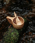 Kuksa Wooden Cup Handcarved 8 Oz Coffee Mug with Lanyard and Carabiner resting on moss by a river, durable hardwood design for outdoors.