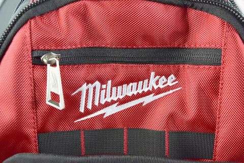 Interior view of red Pro Grade Jobsite Backpack For Tradesmen With Ultra Durable 1680D Fabric, showing logo and zipper pocket.