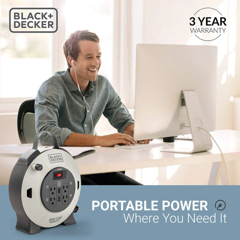 Man using computer near 25 Ft Retractable Extension Cord Reel with 4 outlets, 2 USB ports, multi plug, on off switch.