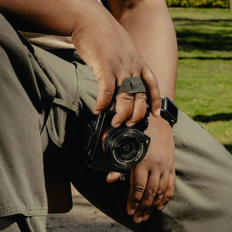 Person holding Micro Clutch L Plate Hand Strap for Mirrorless Cameras Low Profile Finger Loop with Battery Access ARCA Base