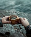 Person holding Kuksa Wooden Cup Handcarved 8 Oz Coffee Mug With Lanyard And Carabiner For Camping Outdoors by a lake