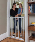 Everywhere Extra Tall and Wide Baby and Pet Gate for Doorways, Halls, and Stairs, Adjustable 28.75 to 39.75 Inch Wide, 36 Inch Tall, Pressure or Hardware Mounted, Easy In-Between Rooms Install, White Metal gate installed in doorway, woman holding child on one side.