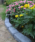 Garden with pink and yellow flowers bordered by Realistic Faux Stone Landscape Edging Kit With 24 Bricks, 15.5 Ft Total.