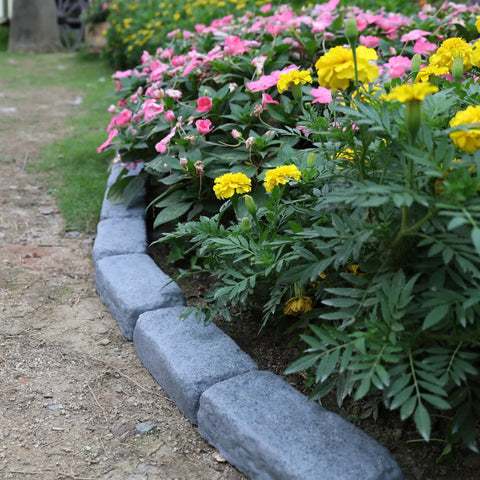 Garden with pink and yellow flowers bordered by Realistic Faux Stone Landscape Edging Kit With 24 Bricks, 15.5 Ft Total.