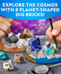 Hands excavating Space Gemstone Dig Kit For Kids With 8 Planet Shaped Bricks And 16 Real Gem And Mineral Specimens on lunar surface.