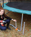 Woman installing Top Shelf 18 Inch Aluminum Screw Earth Anchor for trampoline; reusable, heat-treated, durable design.