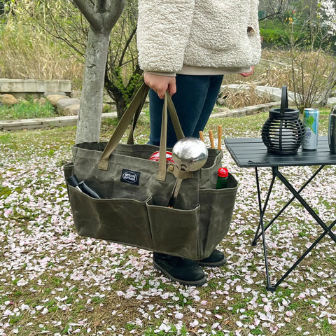 Person holding Waxed Canvas Firewood Carrier Tote For Camping And Garden Work, Collapsible And Sturdy Tool Storage Basket in army green