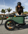 Two 16 By 3 Inch Bike Trailer Wheel Kit With Aluminum Rim And Hub, Steel Spokes, Knobby Tread For All Terrain Traction, Easy Push Button Attachment on bike trailer in use by a person outdoors near other bikes.