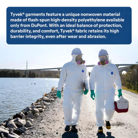 Two workers in cleanroom safety suits and masks walking outdoors by a water body.