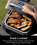 Person grilling meat and vegetables on Woodfire Outdoor Grill And Smoker With Four In One Functionality OG301.