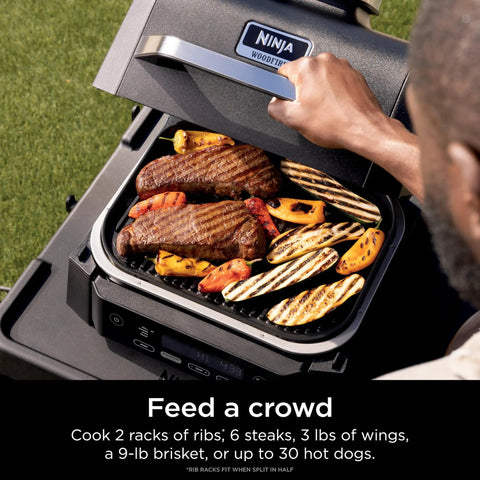 Person grilling meat and vegetables on Woodfire Outdoor Grill And Smoker With Four In One Functionality OG301.