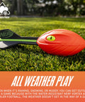 Vortex Aero Howler Foam Football With Mega Distance Passes Flight Tail on grass, showing vibrant orange color and easy grip.