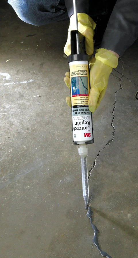 Person applying DP600 Gray Self-Leveling Concrete Repair Sealant Cartridge With 2 Mix Nozzles 8.4 Fl Oz to a concrete crack