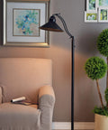 Open Frame Drafting Lamp Style Floor Lamp In Oil Rubbed Bronze beside a chair with artwork on gray wall background.