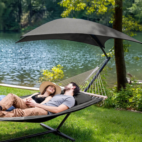 Standing Patio Hammock With Canopy And Foldable Stand, Portable And Easy Setup, Patent Pending, Dark Gray, Two Layer Quilted Polyester Comfort For Camping And Outdoor Kickback Lounging with couple relaxing by a lake.