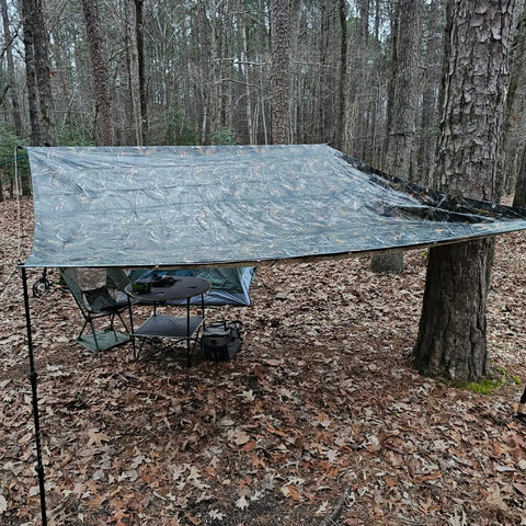 Heavy Duty Waterproof Tarp With Bionic Tree Camo Multi Purpose Poly Cover 8 Mil Thick 10 By 16 Feet For Equipment Machinery Construction Painting And Outdoor Projects set up in a forest