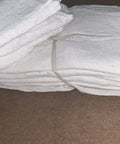 Stack of 2500 Count White Shop Towels For Mechanics, Industrial Grade 14x14, 100 Percent Cotton Rags, on a brown surface.