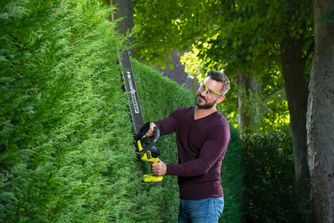 Man using Pro Level 18V ONE PLUS Cordless Hedge Trimmer Featuring 55cm Double Edge Blades trimming a hedge.