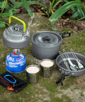 Lightweight Camping Cookware Mess Kit Gear with pot, pan, kettle, two cups, utensils on mossy surface for backpacking, hiking