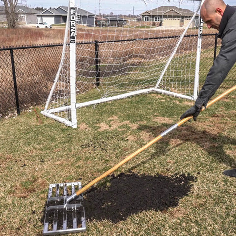 Person using 30-Inch Lawn Leveling Rake With 72-Inch Handle, Stainless Steel Tray, in garden behind soccer goal, effortless garden leveling