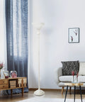 Living room with tall white floor lamp next to sofa and wooden table against decorative wall and curtain background.