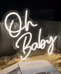 Oh Baby Warm White LED Neon Sign For Home Decor And Party Vibes on a rug with magazine, wall hanging neon light