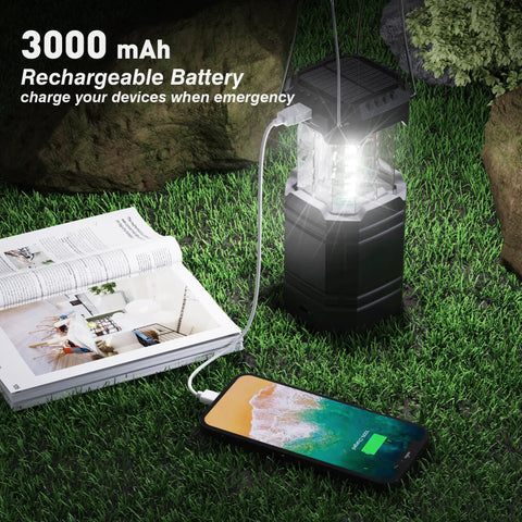 Hand Crank Solar Camping Lantern With 3000mAh Battery, Ultra Bright LED Torch, USB Rechargeable next to phone charging on grass