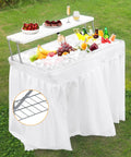 Two Tier Folding Ice Cooler Table With Skirt And Grid Rack Drain Hose Portable Party Table For Patio, Picnic, Camping And Wedding Use Keeps Drinks Cold And Food Fresh White, loaded with fruits and drinks.