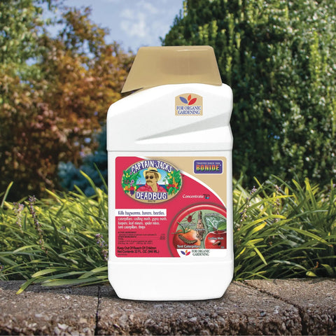 Deadbug Brew Insecticide Concentrate For Outdoor Gardens 32 Oz bottle on garden ledge with trees in background