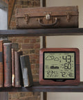 Backlit Wireless Forecast Weather Station With Pressure And Temp Trends Indoor Outdoor Temp Humidity 24 Hour Pressure History Temperature Alerts And Continuous Display on shelf with books and suitcase.