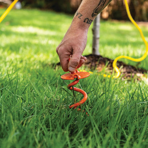 Person installing Heavy Duty 8 Inch Spiral Ground Anchor With Folding Ring Screw In Steel For 125 Lb Pull Weatherproof Powder Coated Orange