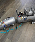 Lightweight Portable Aluminum Air Tank 5 Gallon Rust Free And Easy To Lug 125 PSI Maximum Includes One Quarter Inch Quick Connector Hose And Tire Chuck For Fast Tire Inflation next to air compressor on wooden floor.