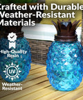 Close-up of blue Tropical Pineapple Glass Patio Torch Set Of 2, showing weather-resistant resin material on a patio table.