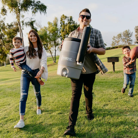 Five Gallon Portable Sports Cooler And Water Dispenser With Flat Seat Lid Tailgate Ready Insulated Beverage Dispenser In Gray And Black Recessed Drip Resistant Spigot Reinforced Handles Lid Keeper UV Protected Infrared Technology outdoors with family.