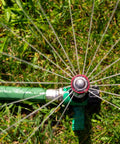 Top view of Pro Grade Hose End Sprinkler with High Efficiency Rotary Pattern on grass, showing water spray and metal spike.