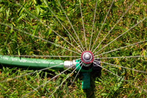Top view of Pro Grade Hose End Sprinkler with High Efficiency Rotary Pattern on grass, showing water spray and metal spike.