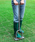 Person using Manual Lawn Aerator Spike Tool With 15 Iron Spikes for soil aeration on grassy lawn area.